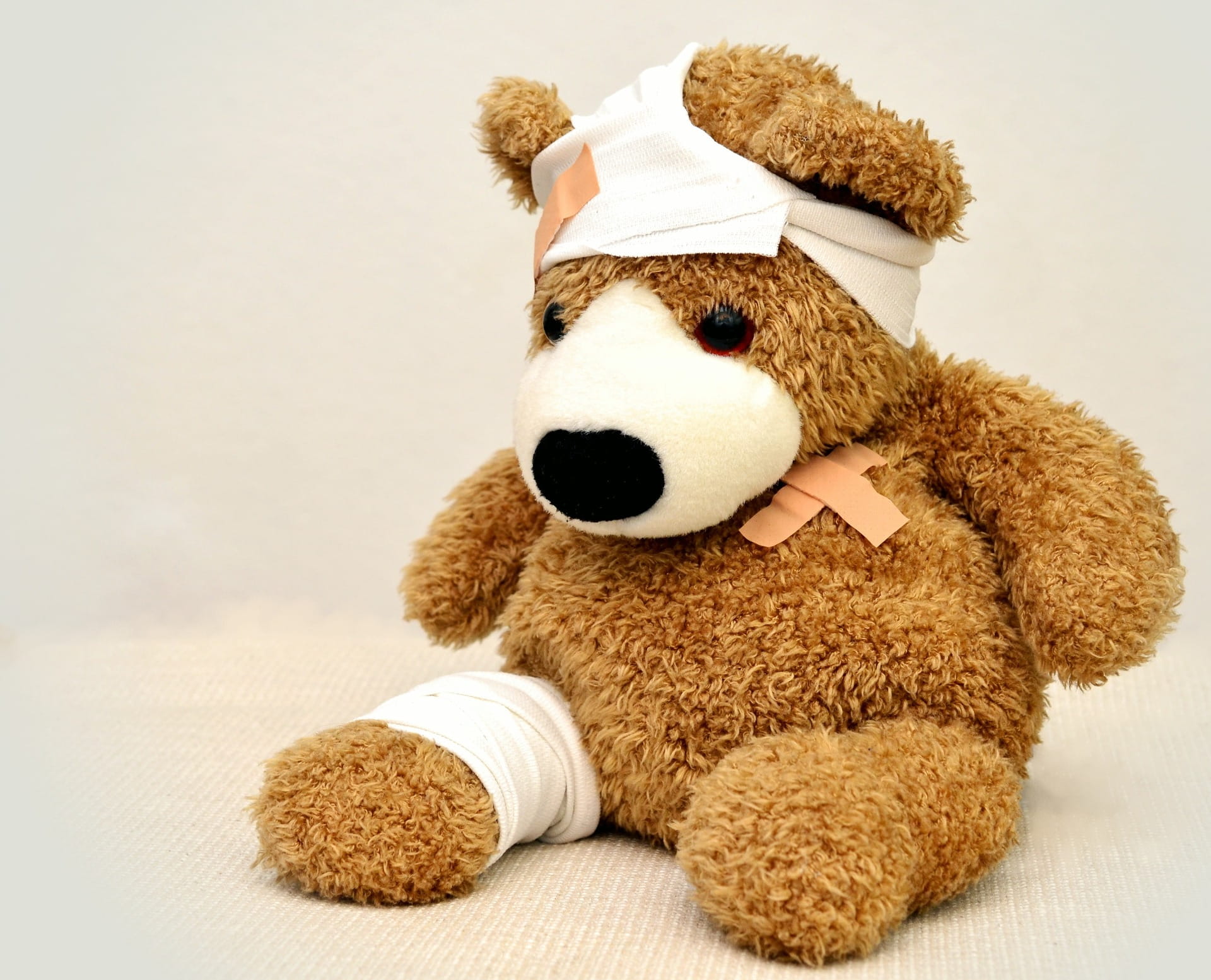 Oso de peluche marrón con gorro blanco y moño rosa, sentado sobre fondo claro. Seguro Accidentes Personales