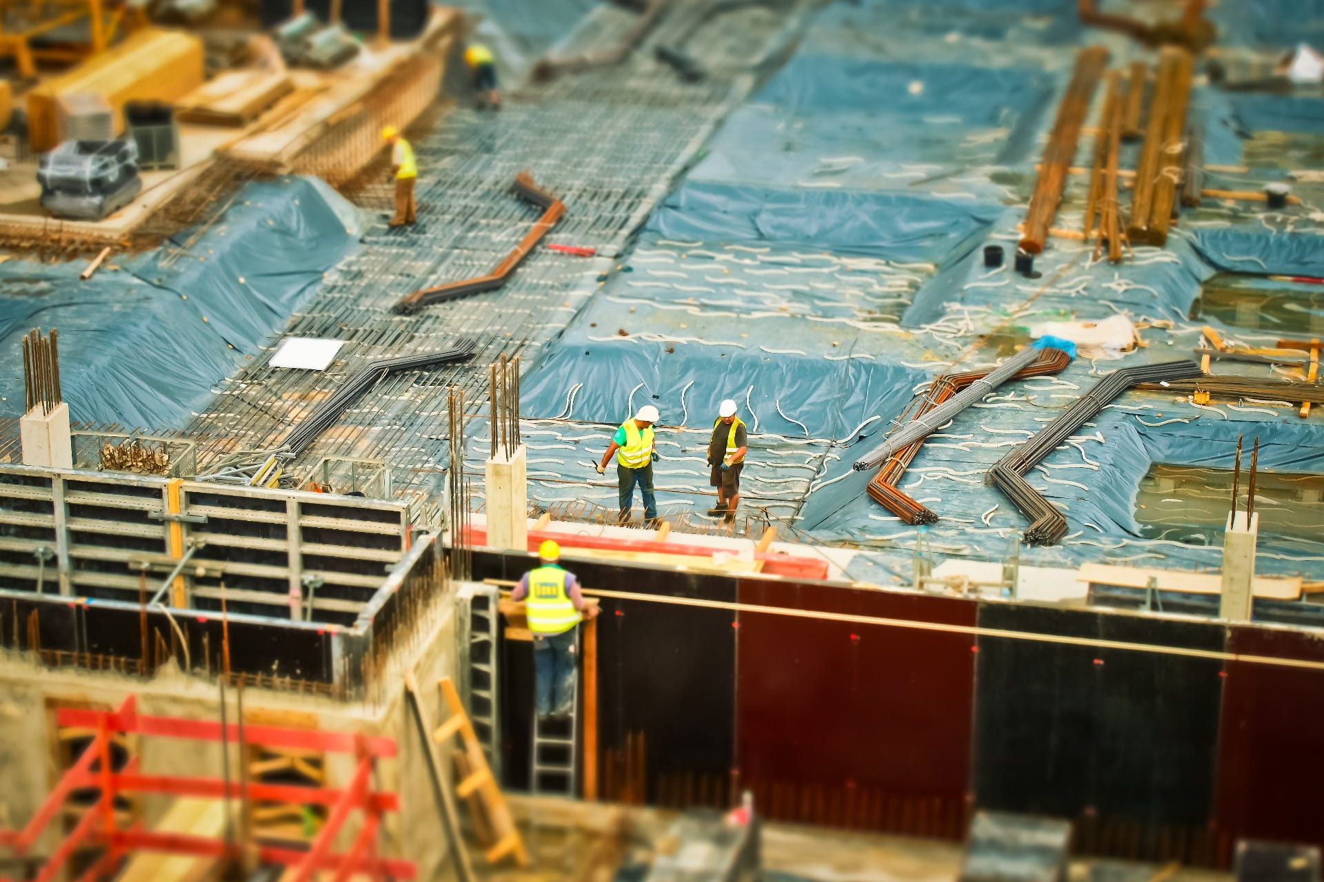 Trabajadores con chalecos y casco inspeccionan una losa de hormigón con armaduras dentro de una obra. Seguros de obra, todo riesgo de construcción y montaje