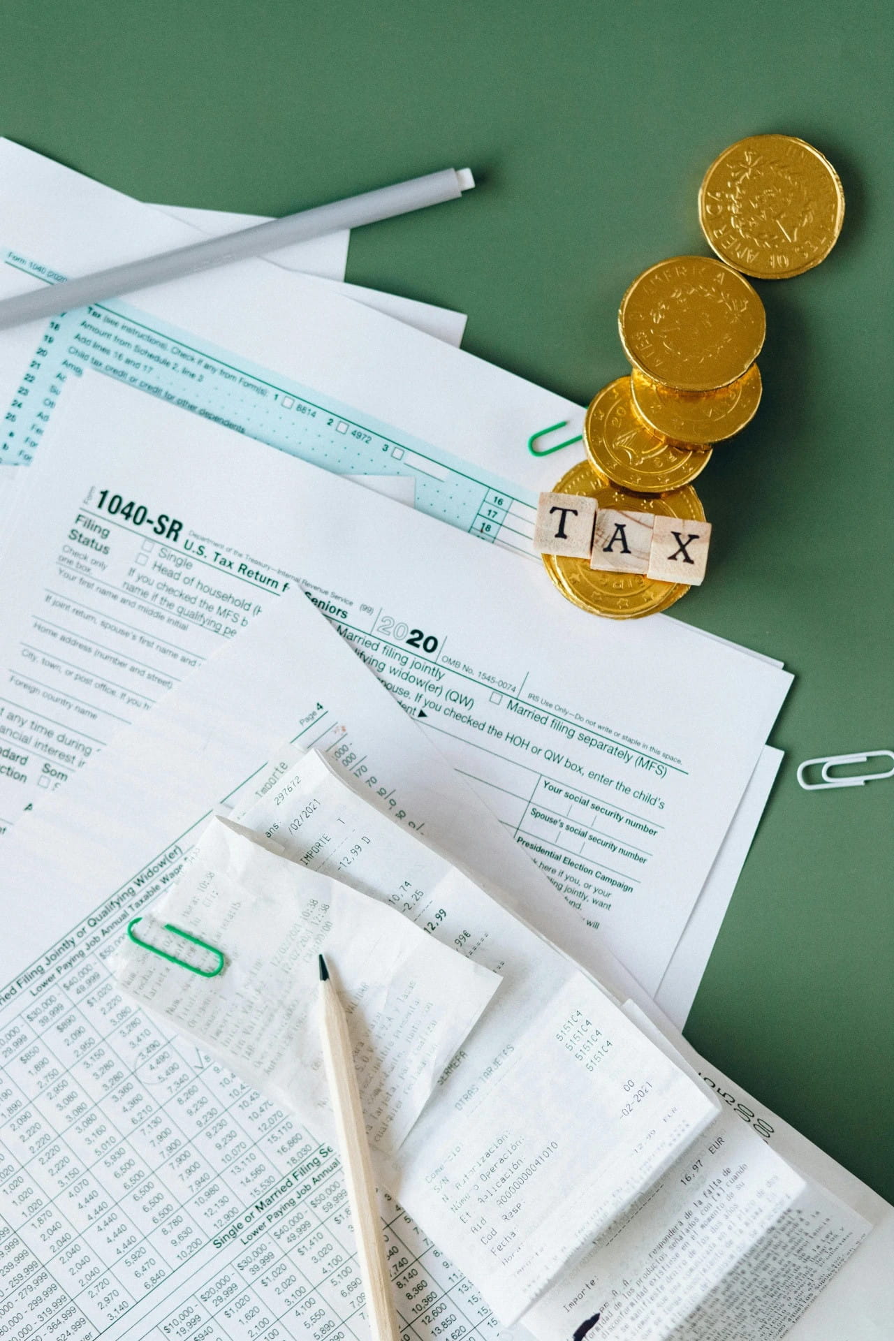 Monedas de oro y formularios de impuestos 1040-SR sobre escritorio verde, con bolígrafo y calculadora. Seguro de Crédito
