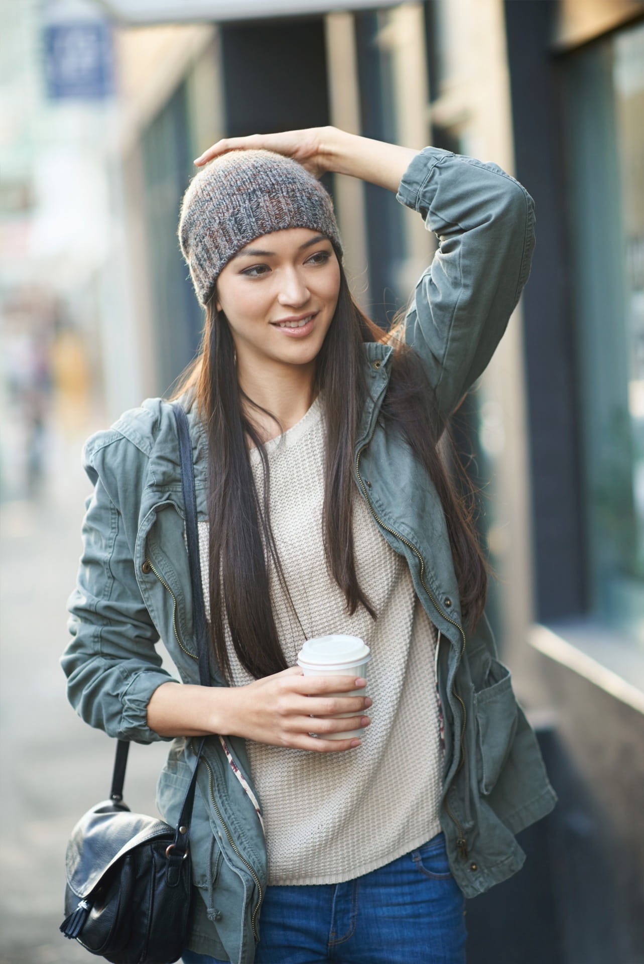 Mujer sonriente con gorro de lana y chaqueta verde, sostiene café y se toca la cabeza. Seguro catastrófico individual